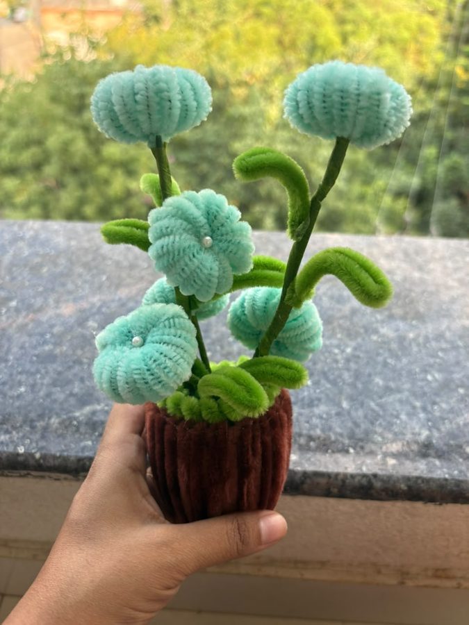 Aqua Bloom Pot. Handcrafted potted bouquet made from soft chenille wire, with mint-blue flowers, pearl centers, and curly green leaves. Set in a brown knitted pot. A fresh, calming accent for any desk or shelf.