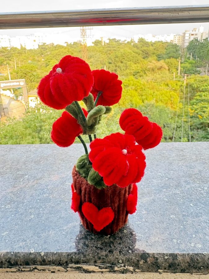 Crimson Heart Bloom Pot. Handcrafted potted bouquet made from soft chenille wire, with bold red flowers, pearl centers, and green leaves. Set in a brown knitted pot decorated with red hearts. A romantic gift for any d…