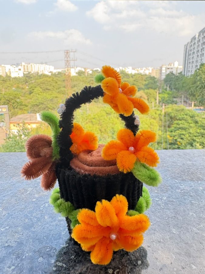 An orange chenille flower basket with a black handle and a knitted base.