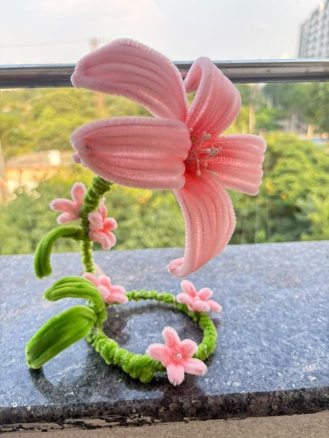 Pink Lily Stand. Handcrafted pink lily made from soft chenille wire, with a large curved bloom, small blossoms, and green leaves. Stands on a round green ring base. An elegant showpiece for any desk or shelf.