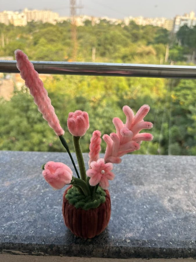 Rose Meadow Pot. Handcrafted potted bouquet made from soft chenille wire, with pink tulips, a blossom, and feathery spikes on green stems. Set in a brown knitted pot with a green moss top. A gentle accent for any desk…