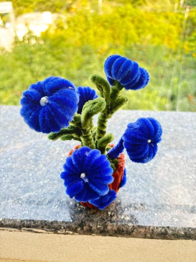 Royal Blue Bloom Pot. Handcrafted potted bouquet made from soft chenille wire, with deep blue flowers, pearl centers, and curly green stems. Set in a small orange-brown knitted pot. A vivid accent for any desk or shelf.