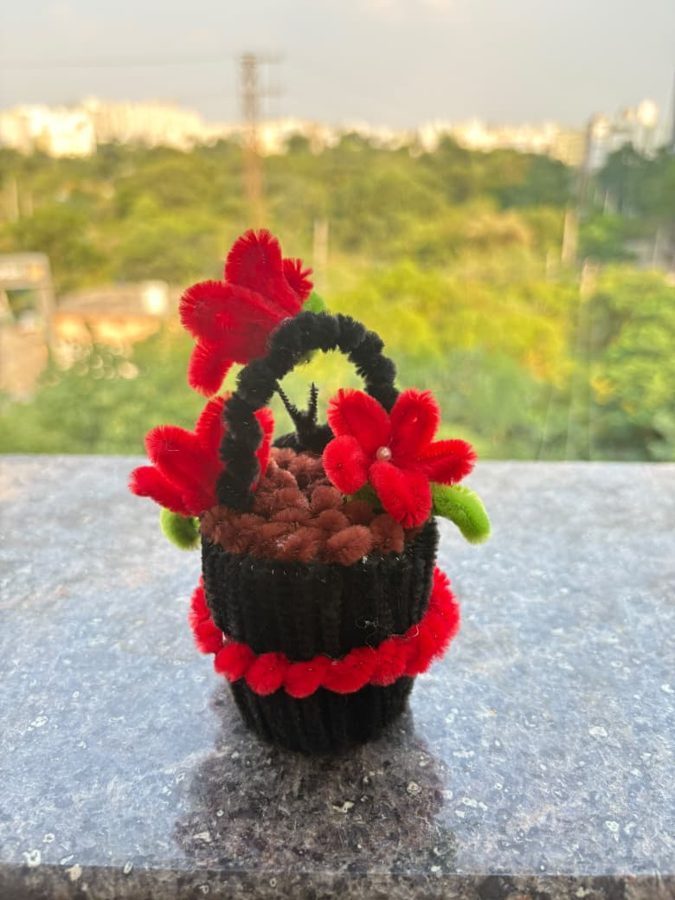 Scarlet Mini Basket. Handcrafted mini flower basket made from soft chenille wire, with red blossoms, a pearl center, and green leaves. Finished with a black handle and a red-trimmed knitted base. A bold little gift fo…